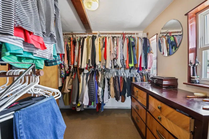 Slide: The Image of Walk-in closet with hanging clothes, wooden dresser, and round mirror. - 33