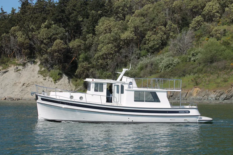 Slide: The Image of 2025 Nordic Tug 40 cruising near a forested shoreline. - 1