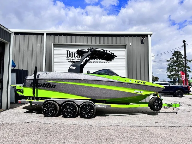 Slide: The Image of 2016 Malibu M235 boat in green and gray on a trailer outside a dockside facility. - 0