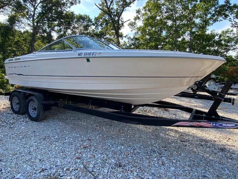 Slide: The Image of 2001 Bayliner 215 Bowrider on a trailer, parked on gravel with trees in the background. - 28