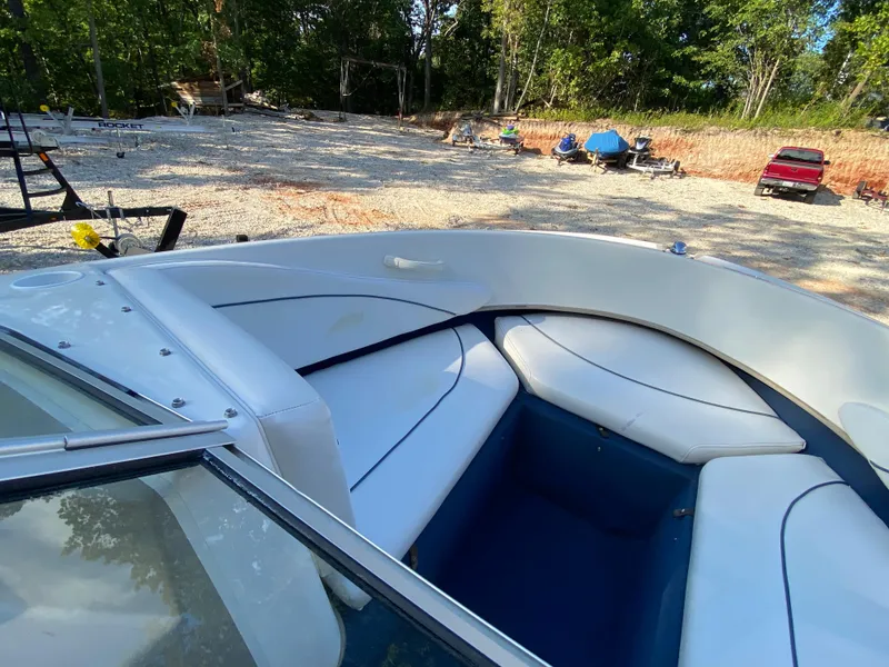 Slide: The Image of 2001 Bayliner 215 Bowrider boat with white and blue interior, parked on a gravel lot. - 5