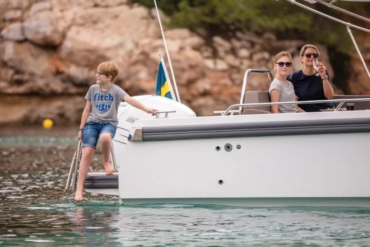 Slide: The Image of Family enjoying a day on a Nimbus W9 boat, 2025 model, near rocky shoreline. - 45