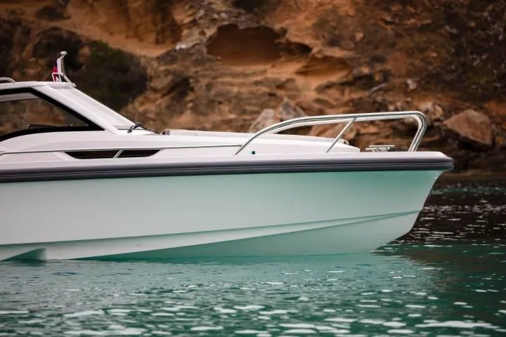 Slide: The Image of 2025 Nimbus W9 boat cruising in clear turquoise waters near rocky shoreline. - 46