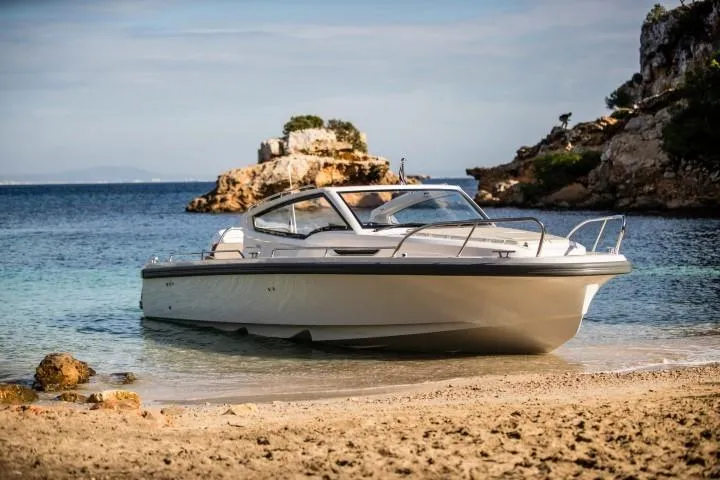 Slide: The Image of 2025 Nimbus W9 boat anchored on a sandy beach with rocky cliffs in the background. - 21