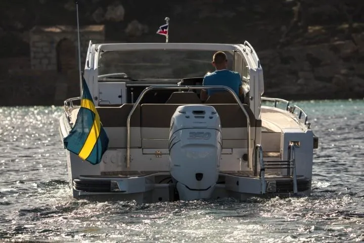 Slide: The Image of Nimbus W9 2025 motorboat cruising on water, rear view with flag. - 4