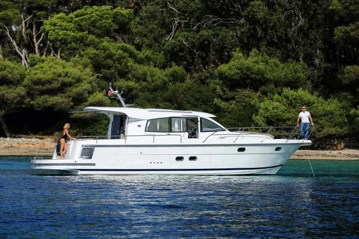 The Image of 2024 Nimbus 405 Coupé yacht cruising near a forested shoreline. - 0