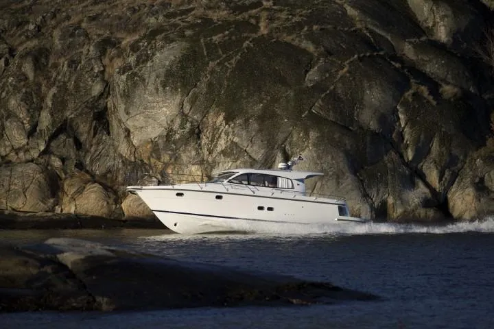 Slide: The Image of Nimbus 405 Coupé 2025 yacht cruising near rocky shoreline. - 1