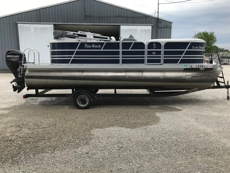 Slide: The Image of 2015 Palm Beach Ultra Sport 220 pontoon boat on trailer, parked outside a warehouse. - 1