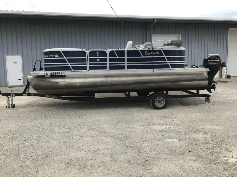 Slide: The Image of 2015 Palm Beach Ultra Sport 220 pontoon boat on trailer, parked outside a metal building. - 8