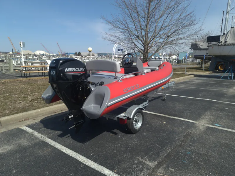 Slide: The Image of 2023 Grand Inflatables G380EF boat with Mercury engine on trailer in parking lot. - 2