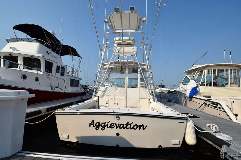 Slide: The Image of 2007 Carolina Classic 28 Express boat docked, named "Aggievation," with fishing tower and neighboring vessels. - 7