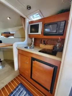 Slide: The Image of 2006 Rinker 300 Express Cruiser interior with kitchenette, featuring sink, microwave, and wooden cabinetry. - 14