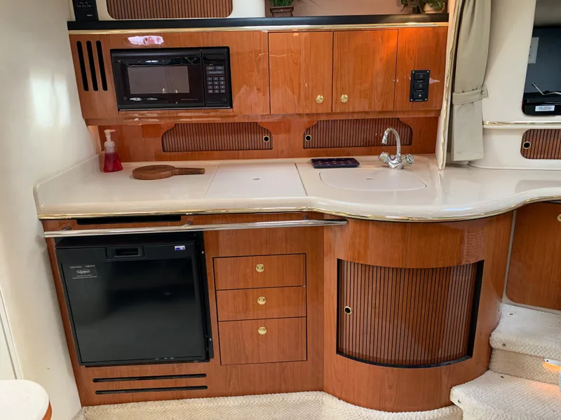 Slide: The Image of 2001 Sea Ray 310 Sundancer kitchen with wood cabinets, microwave, sink, and mini fridge. - 10