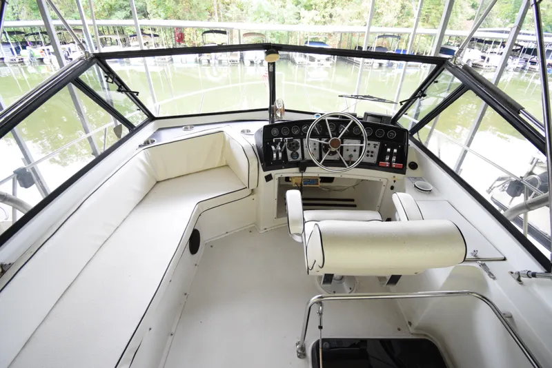 Slide: The Image of 1989 Carver 32 Mariner boat cockpit with white seating and steering wheel, docked near water. - 11
