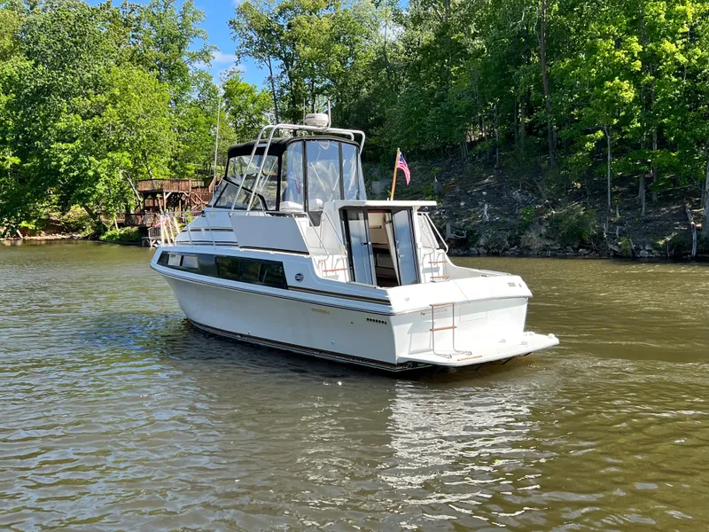 Slide: The Image of 1989 Carver 32 Mariner boat cruising on a scenic river with lush greenery. - 2