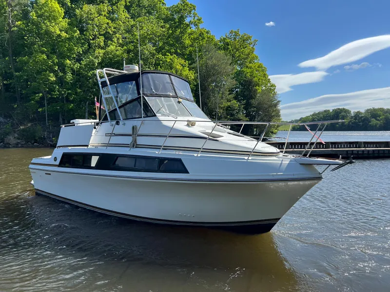 Slide: The Image of 1989 Carver 32 Mariner boat on a calm lake with lush green trees. - 4