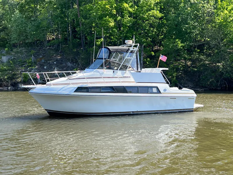 The Image of 1989 Carver 32 Mariner boat on a calm river with lush green trees. - 0