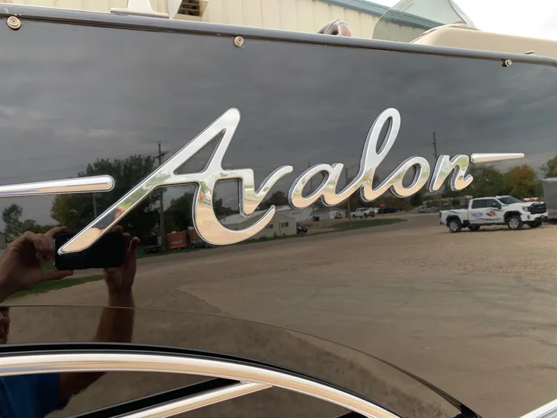 Slide: The Image of 2015 Avalon Ambassador Rear J Lounge boat logo on sleek black surface. - 6