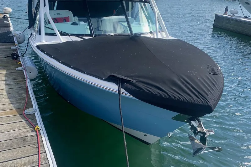 Slide: The Image of 2022 Cobia 240 DC boat docked, covered with a black tarp, in calm waters. - 4