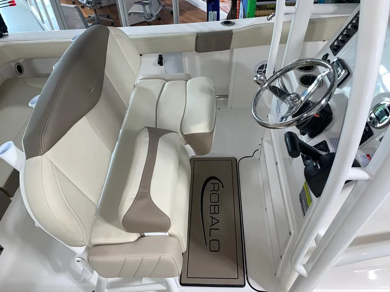 Slide: The Image of 2024 Robalo R222 Explorer boat interior with beige and white seating, steering wheel, and branded mat. - 10
