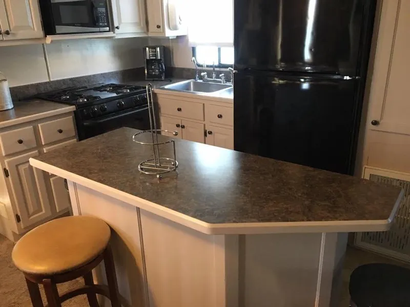 Slide: The Image of 1996 Stardust Cruisers kitchen with island, black appliances, and white cabinetry. - 12