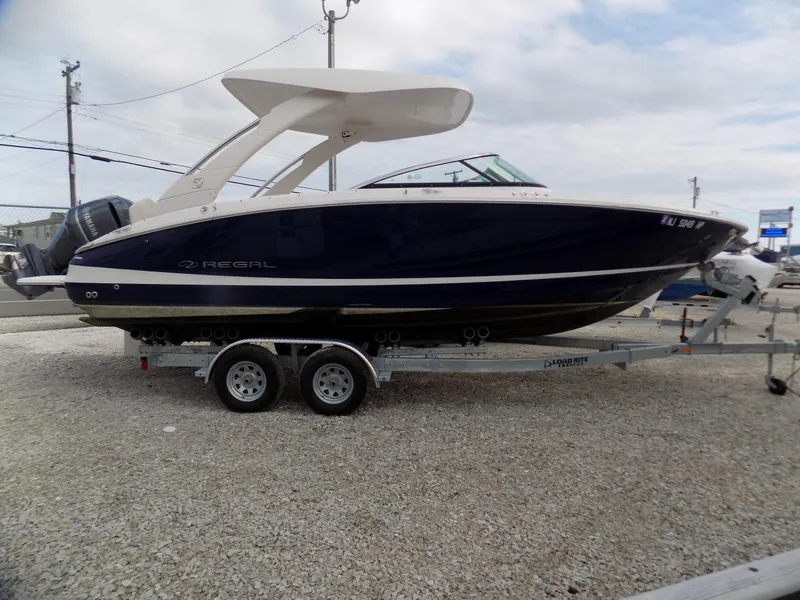 Slide: The Image of 2021 Regal LX6 boat on trailer, parked on gravel, under cloudy sky. - 1