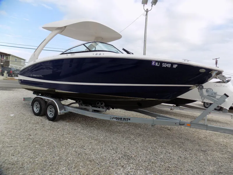Slide: The Image of 2021 Regal LX6 boat on trailer, parked on gravel, under cloudy sky. - 2