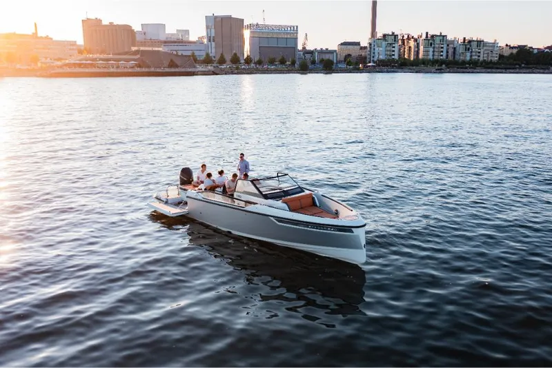 Slide: The Image of 2023 Saxdor 320 GTR boat cruising on a calm urban waterfront at sunset. - 10