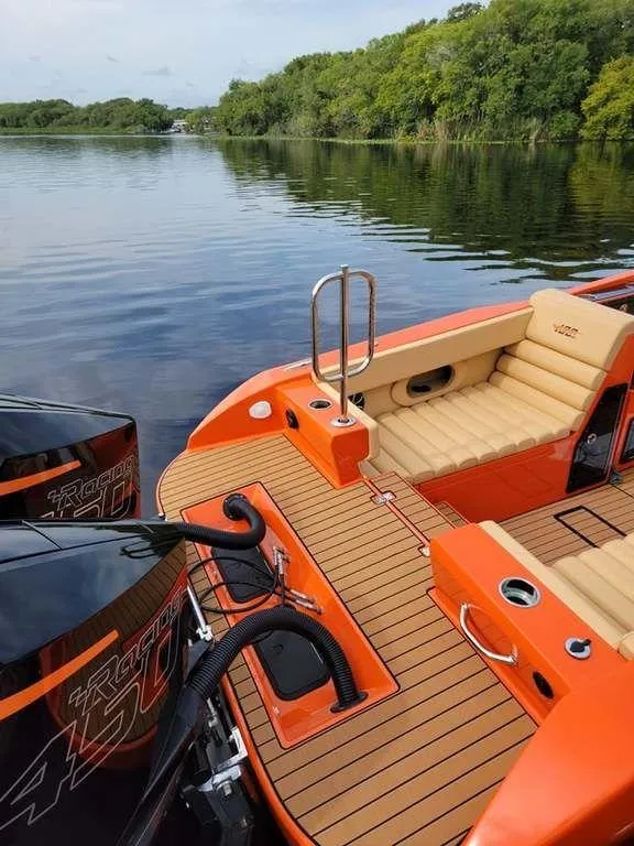 Slide: The Image of 2024 Velocity 430VRX boat with orange deck and twin engines on a serene lake. - 4