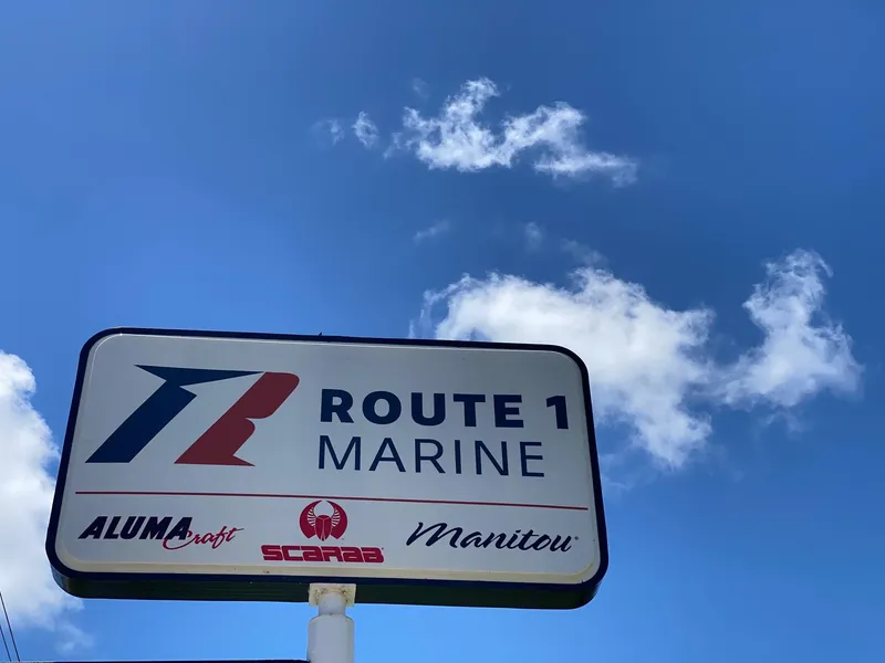 Slide: The Image of Route 1 Marine dealership sign under blue sky, featuring Alumacraft, Scarab, and Manitou brands. - 19