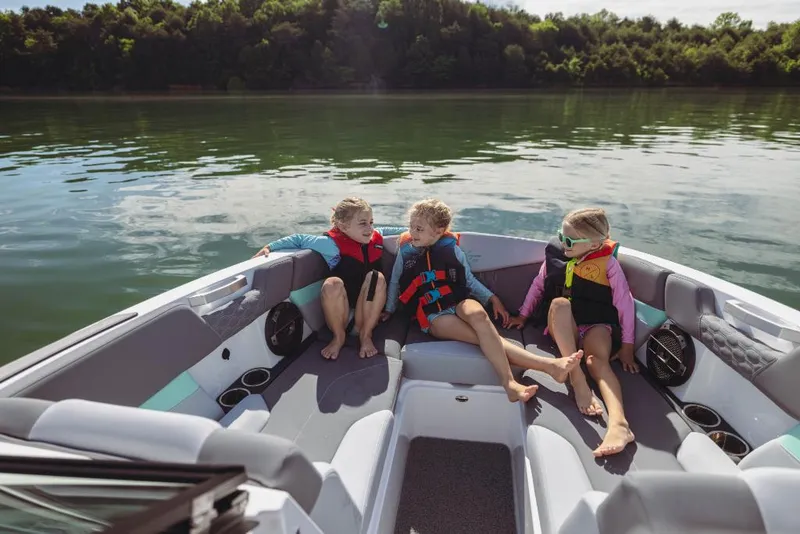 Slide: The Image of Children enjoying a ride on a 2023 MasterCraft XT24 boat on a serene lake. - 16