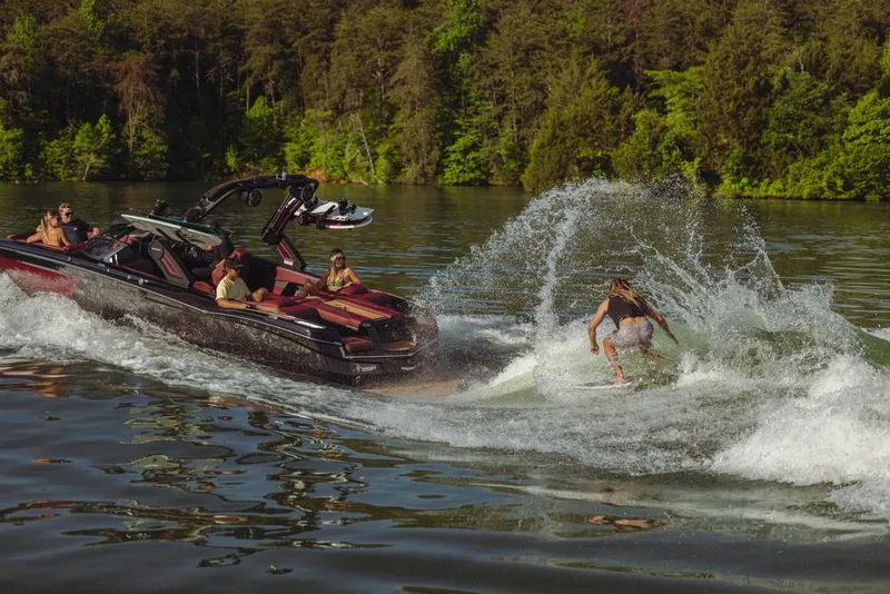 Slide: The Image of 2023 MasterCraft XStar S boat towing a wakeboarder on a scenic lake. - 1