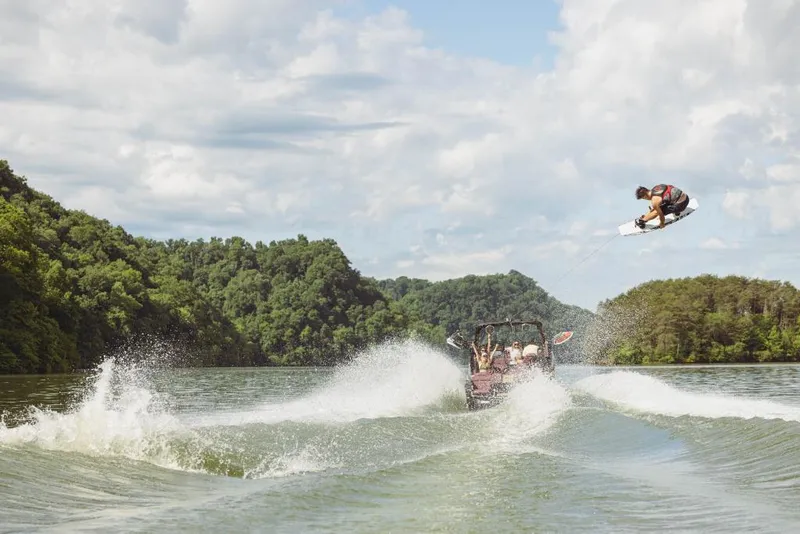 Slide: The Image of Wakeboarder performing a high jump behind a 2023 MasterCraft XStar S boat on a scenic lake. - 17
