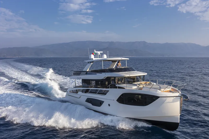 Slide: The Image of 2025 Absolute Navetta 64 yacht cruising on open sea with scenic mountain backdrop. - 1