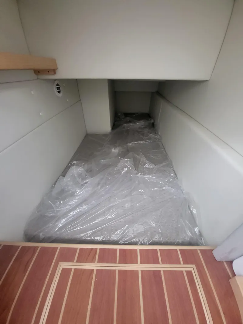 Slide: The Image of 2024 ArrowCat 320 interior cabin with plastic-covered bed and wooden flooring. - 8