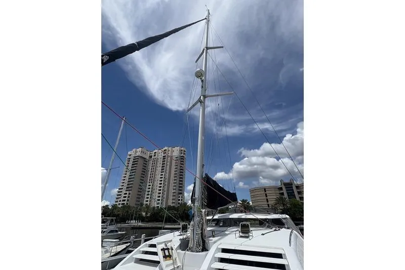 Slide: The Image of 1998 Leopard Catamaran with tall mast, docked near urban high-rise buildings under a cloudy sky. - 73