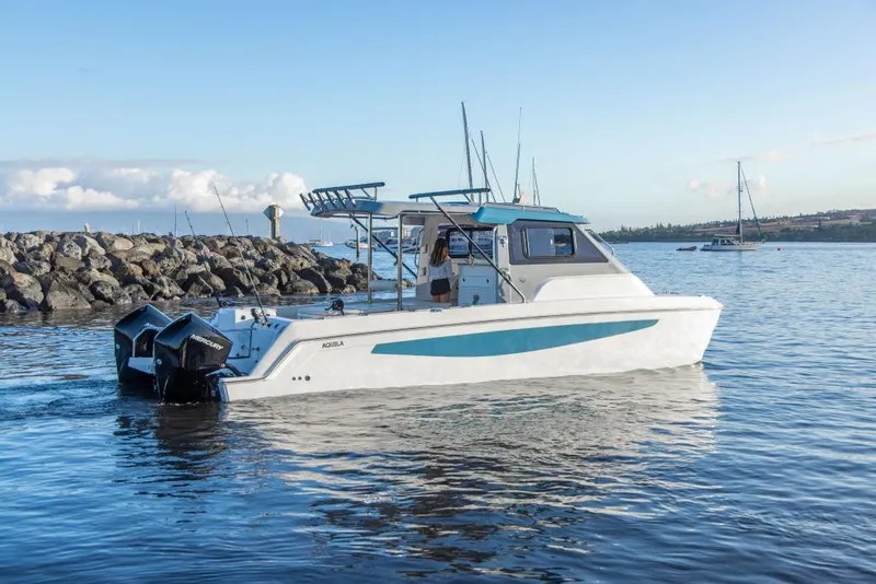 Slide: The Image of 2023 Aquila 28 Molokai Cuddy boat on calm water near rocky shore. - 2