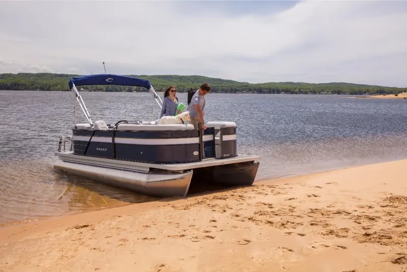 Slide: The Image of 2023 Crest Classic LX pontoon boat beached on a sandy shore with two people onboard. - 13