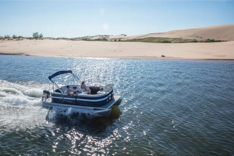 Slide: The Image of 2023 Crest Classic LX boat cruising on a sunny lake near sandy dunes. - 5