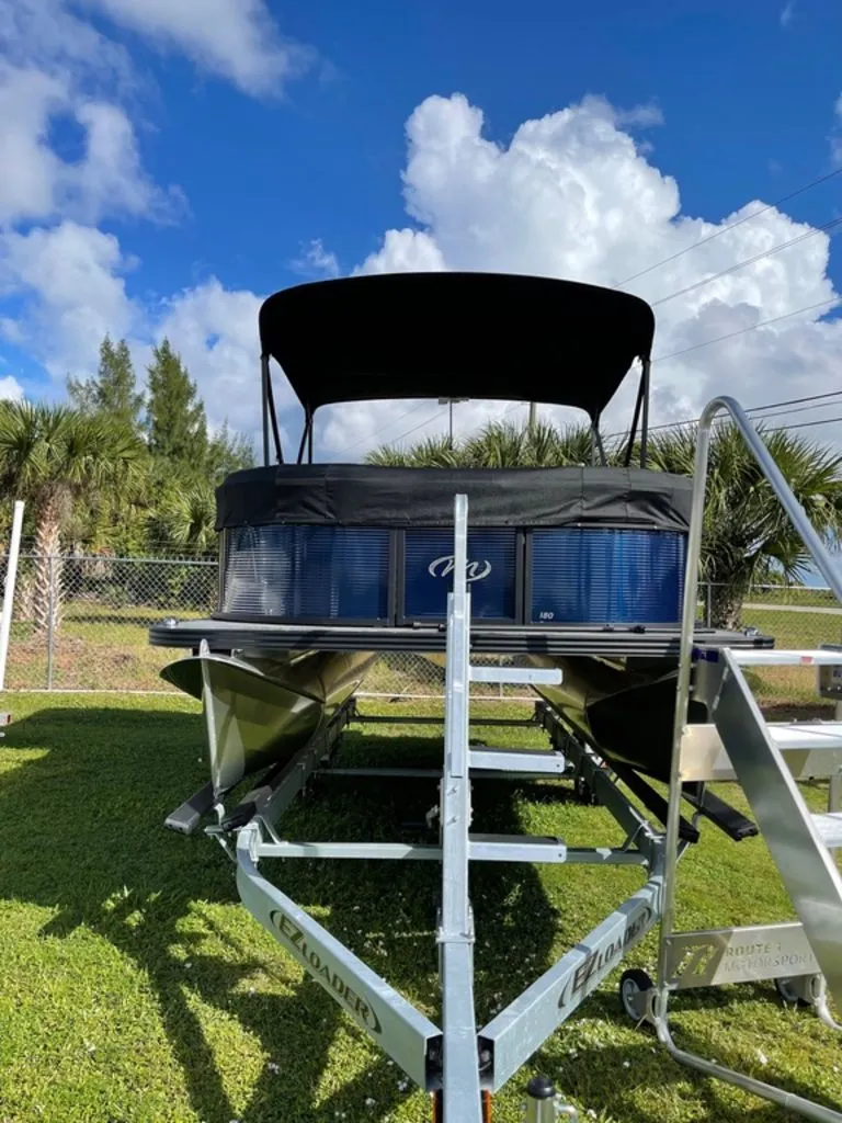 Slide: The Image of 2022 Manitou 18 Aurora LE Twin Tube 25 pontoon boat on trailer under blue sky. - 2
