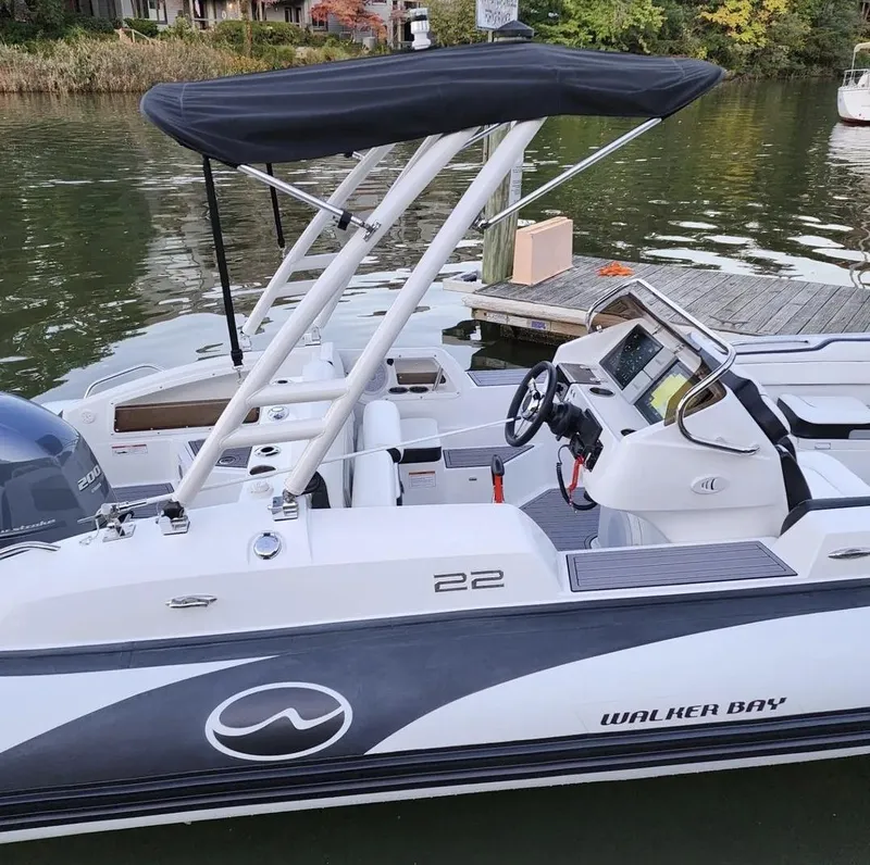 Slide: The Image of 2025 Walker Bay WB 22 boat docked by a lake with a black canopy. - 1