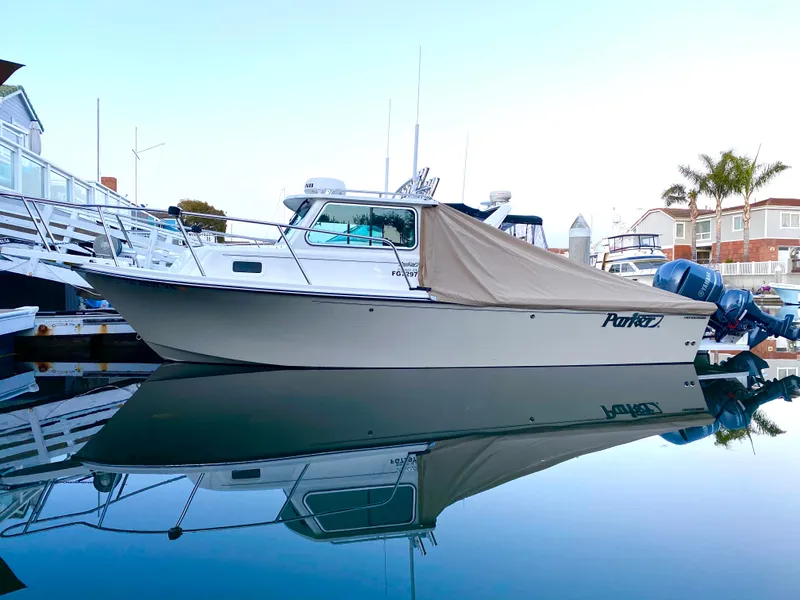 Slide: The Image of 2017 Parker 2320 Sport Cabin boat docked with cover, calm water reflection. - 18