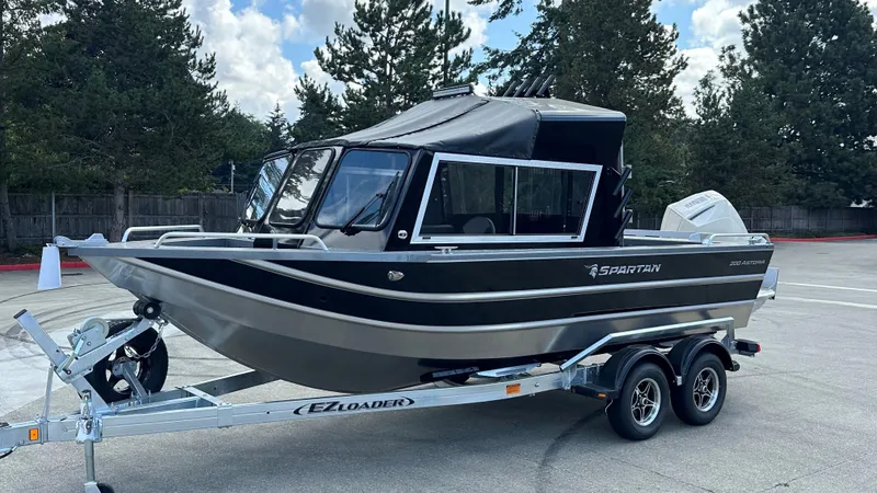Slide: The Image of 2024 Spartan 200 Astoria boat on trailer, parked outdoors with trees in background. - 33