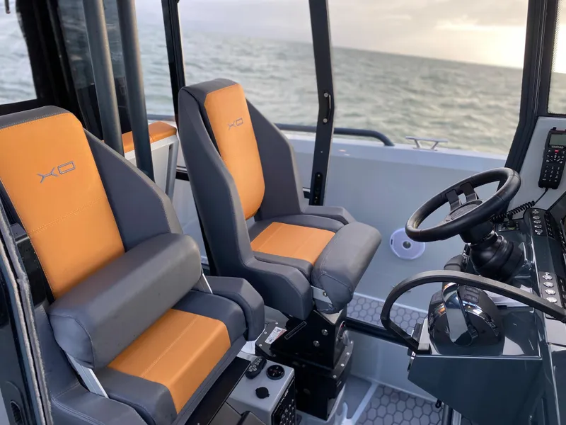 Slide: The Image of 2023 XO Boats Defender 9 interior with orange and gray seats, steering wheel, and ocean view. - 14