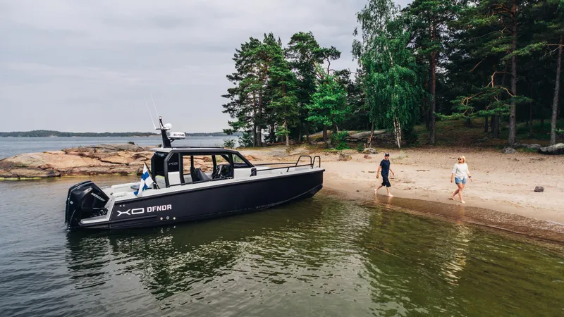 Slide: The Image of 2023 XO Boats Defender 9 docked on a scenic beach with people walking nearby. - 3
