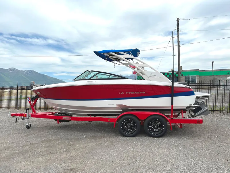 Slide: The Image of 2022 Regal LS2 Surf boat on a red trailer, parked outdoors. - 0
