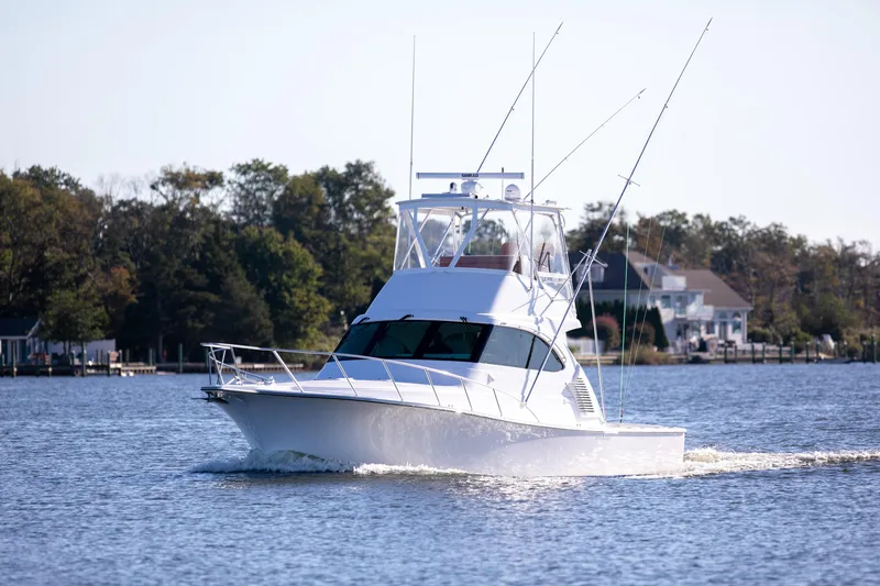 Slide: The Image of 2025 Henriques 42 EXHTB boat cruising on a calm lake near waterfront homes. - 2