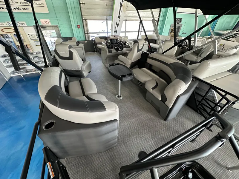 Slide: The Image of 2025 Sylvan Mirage L-1 LZ pontoon boat with canopy and seating, displayed indoors. - 4
