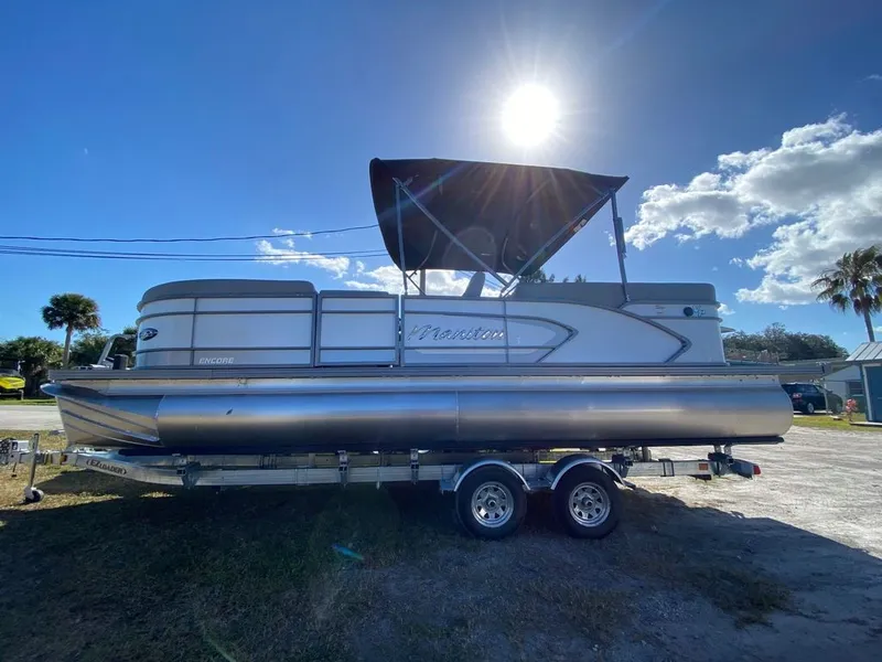 Slide: The Image of 2022 Manitou 23 Encore RF VP pontoon boat on a trailer under a sunny sky. - 3