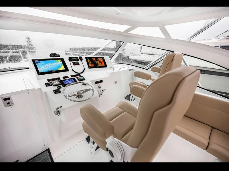 Slide: The Image of 2025 Albemarle 410 Express Fisherman helm with modern navigation displays and beige captain chairs. - 24